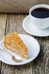 Tasty honey cake with cup of coffee on wooden background.
