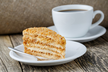 Tasty honey cake with cup of coffee on wooden background.