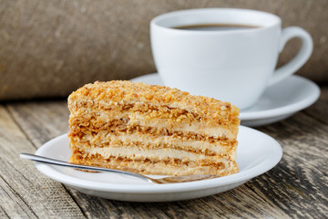 Tasty honey cake with cup of coffee on wooden background.