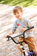Fototapeta na wymiar Smiling boy riding bike with bottle of water