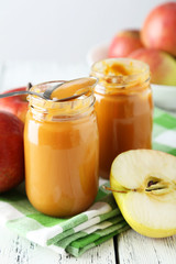 Jars of baby puree with apples on white wooden background