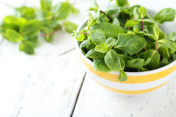 Fresh mint in bowl on white wooden background