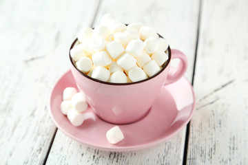 Marshmallows in pink cup on white wooden background