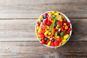 Different fruit candies in bowl on grey wooden background