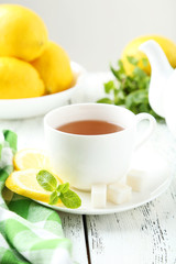 Cup of tea with mint and lemon on white wooden background