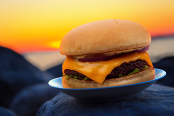 Cheese burger on beach rock in evening sunset