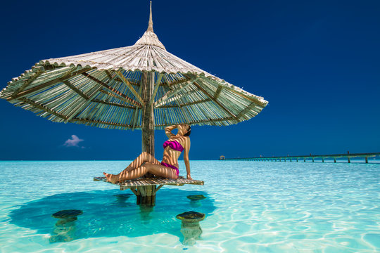 Young beautiful woman in bikinis under beach umbrella in the oce