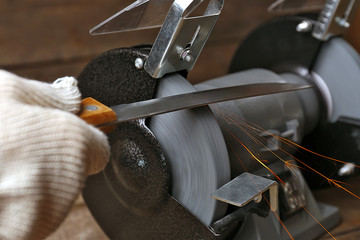 Obraz premium Knife sharpener and hand with blade on wooden table, closeup