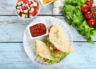 Tasty taco with tomato dip on plate and vegetables on table close up