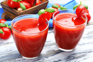 Glasses of tomato juice with vegetables on wooden background