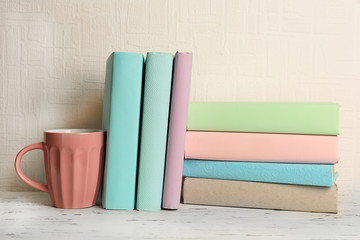 Books and cup on wooden shelf on wallpaper background