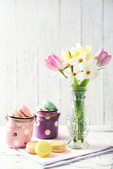 Spring bouquet in vase and tasty macaroons on color wooden background