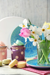 Spring bouquet in glass mug  and tasty macaroons on color wooden background