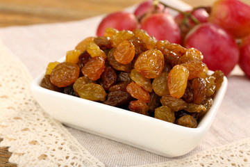 Raisins in bowl with grapes on table close up