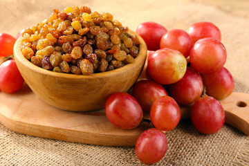 Raisins in bowl with grapes on table close up