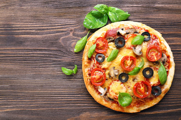 Tasty pizza with vegetables and basil on wooden background