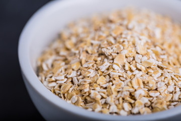 Oatmeal flakes in a white bowl on a black background