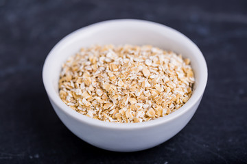 Oatmeal flakes in a white bowl on a black background
