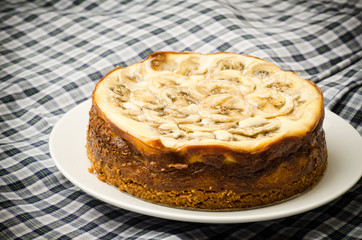 Banana caramel cheesecake on white plate and beautiful fabric