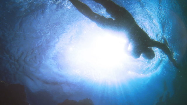 Slow motion Swimming man silhouette with sun rays from bottom camera