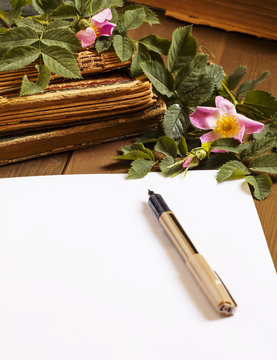 Old books, blank paper, flowers of wild roses in vintage style,