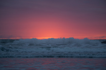 Obraz premium Pacific ocean bright orange and red sunset behind ocean waves.