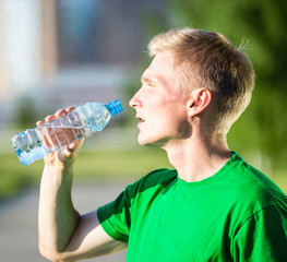 Fototapeta na wymiar Tired man drinking water from a plastic bottle after fitness