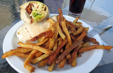 A chicken Caesar wrap served with French fries out on the patio.