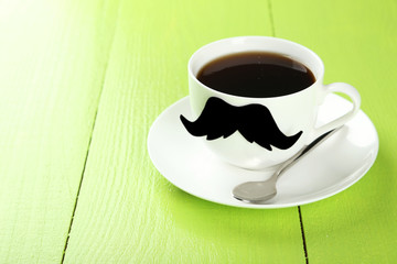 White cup with paper mustache on green wooden background