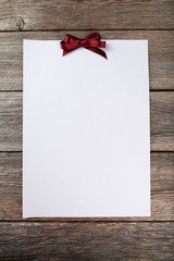 Blank paper sheet with burgundy bow on grey wooden background