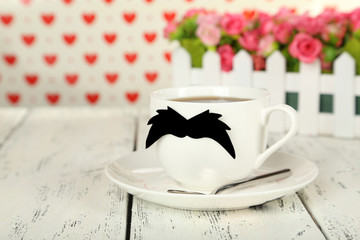 White cup with paper mustache on white wooden background