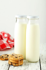 Two bottles of milk and cookies on white wooden background