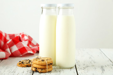 Two bottles of milk and cookies on white wooden background