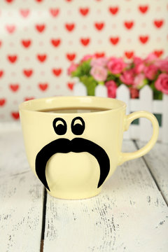 Yellow cup with paper mustache on white wooden background