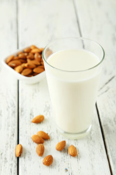 Glass of milk with almonds on white wooden background