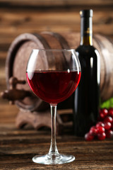 Red wine glass with bottle and barrel on brown wooden background
