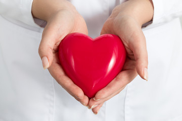 Female doctors's hands holding and covering red heart