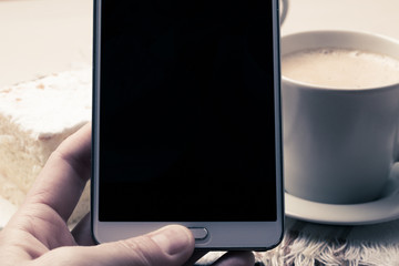 Hand holds mobile phone in front of coffee cup
