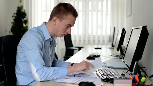 young handsome man works on desktop computer and reads document in the office