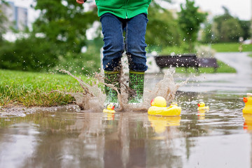 Little boy, jumping in muddy puddles in the park, rubber ducks i