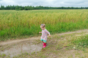 Blonde curly preschooler girl playing on farm dirt road near