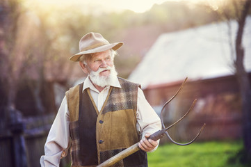 Old farmer with pitchfork in his backyard