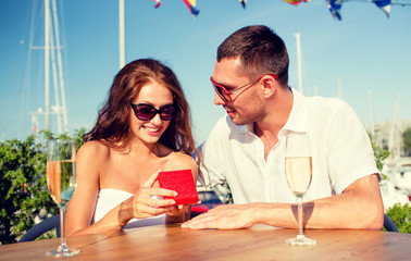 smiling couple with champagne and gift at cafe