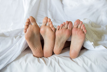 Bare feet of a couple together in a bed, bedding comfort, sleep quality or sex life concept