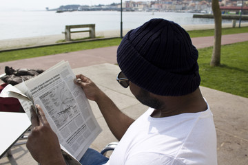 Naklejka premium black man reading newspaper on the terrace
