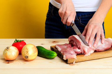 Woman's hands is cutting pork on wooden table