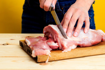 Closeup woman in the kitchen is cutting pork on cutting board