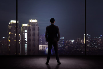 Fototapeta na wymiar Man standing in his office looking at the city at night