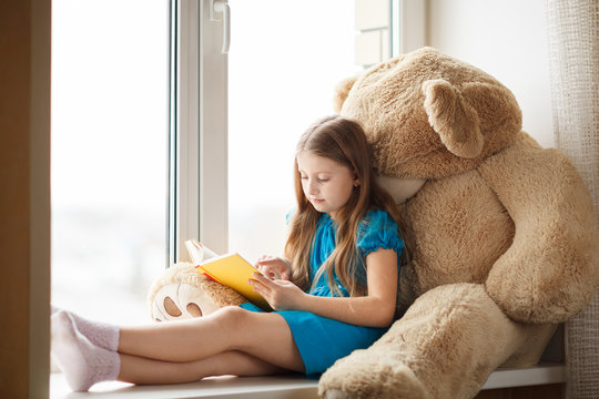 Little girl reading on windowsill with big toy