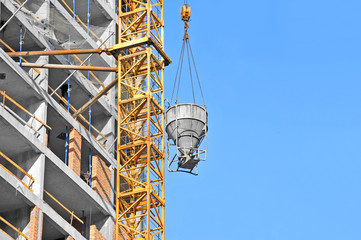Crane lifting concrete mixer container against blue sky